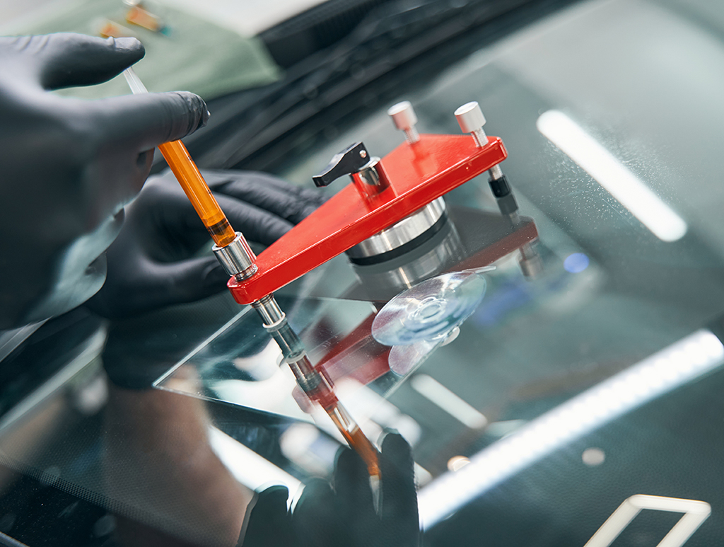Autoglasreparatur -Angestellt in der Karosseriewerkstatt beim Reparieren von kaputten Autoscheiben mit Vakuumspachtel - Autoglasreparatur